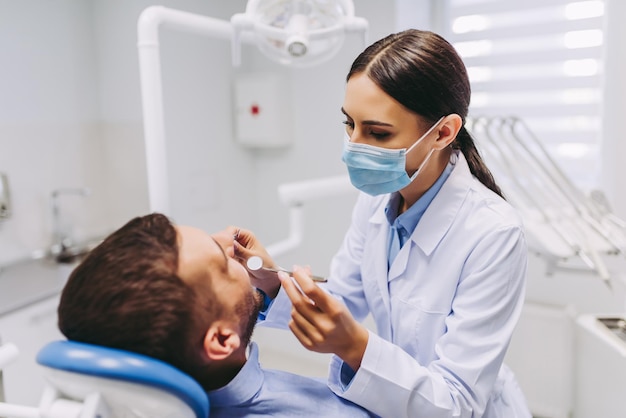 Mujer dentista revisando los dientes del paciente con espejo en la clínica dental moderna
