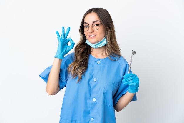 Foto mujer dentista rumano sosteniendo herramientas sobre aislado en la pared rosa mostrando ok firmar con los dedos