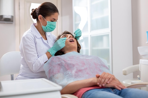 Mujer dentista sondeando los dientes de sus pacientes masculinos con instrumentos dentales