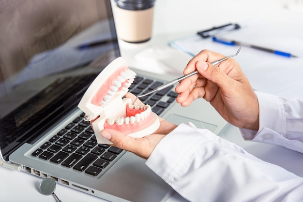 Mujer dentista sosteniendo una herramienta de estomatología profesional y señalando el modelo de diente y explicando al paciente