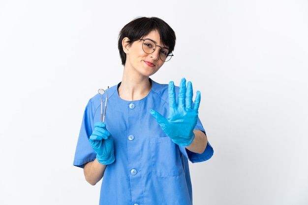 Mujer dentista sosteniendo herramientas aisladas en espacio rosa contando cinco con los dedos