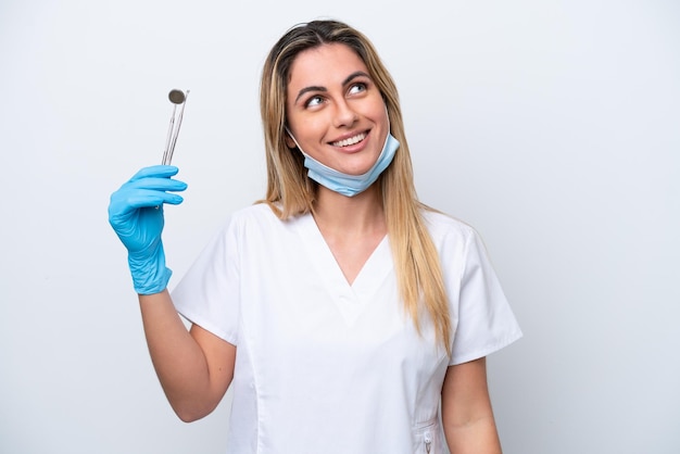 Mujer dentista sosteniendo herramientas aisladas en fondo blanco pensando en una idea mientras mira hacia arriba