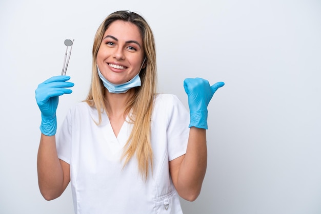 Mujer dentista sosteniendo herramientas aisladas sobre fondo blanco apuntando hacia un lado para presentar un producto