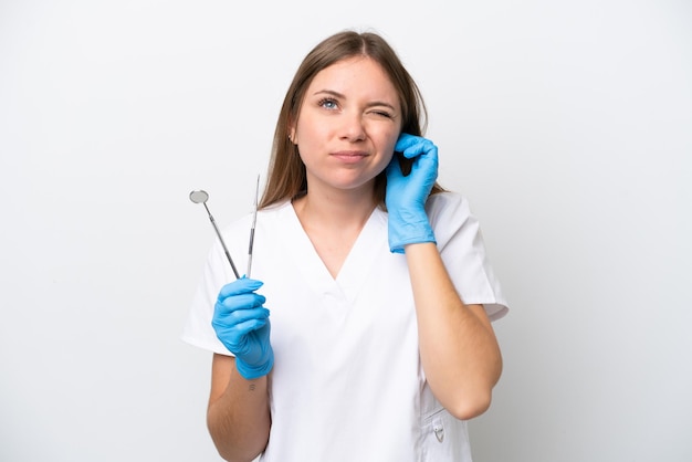 Mujer dentista sosteniendo herramientas aisladas sobre fondo blanco frustrada y cubriendo las orejas