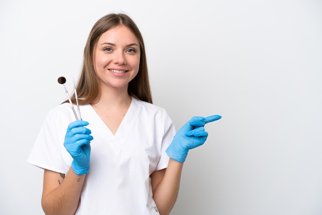 Mujer dentista sosteniendo herramientas aisladas sobre fondo blanco señalando con el dedo hacia un lado