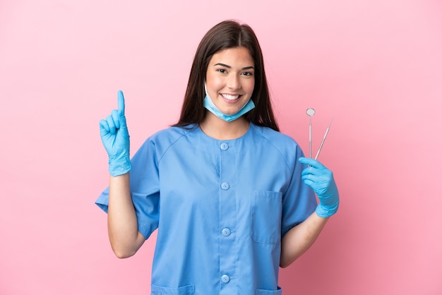 Mujer dentista sosteniendo herramientas aisladas sobre fondo rosa apuntando hacia una gran idea