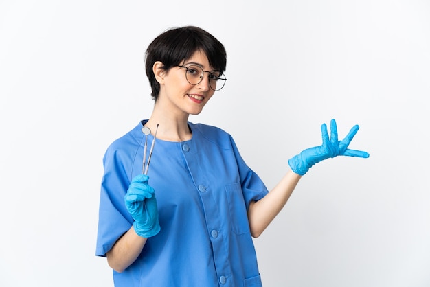 Mujer dentista sosteniendo herramientas aisladas sobre fondo rosa extendiendo las manos hacia el lado para invitar a venir