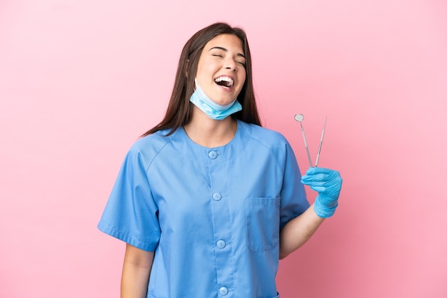 Mujer dentista sosteniendo herramientas aisladas sobre fondo rosa riendo