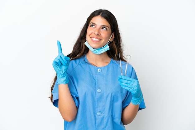 Mujer dentista sosteniendo herramientas sobre fondo blanco aislado apuntando hacia una gran idea