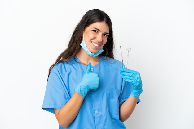 Mujer dentista sosteniendo herramientas sobre fondo blanco aislado dando un gesto de pulgar hacia arriba