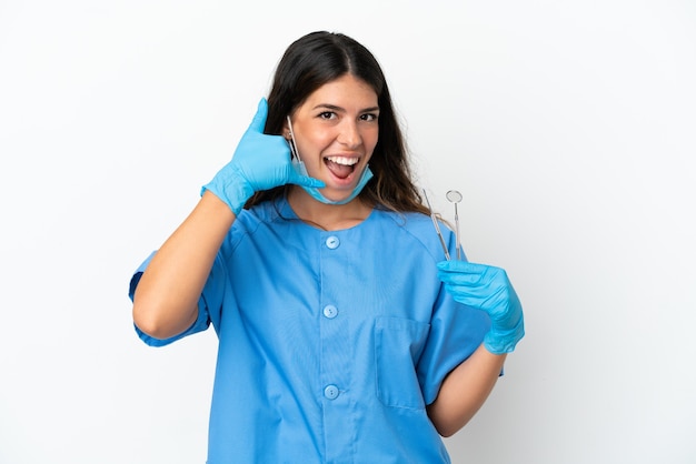 Mujer dentista sosteniendo herramientas sobre fondo blanco aislado haciendo gesto de teléfono. Llámame señal