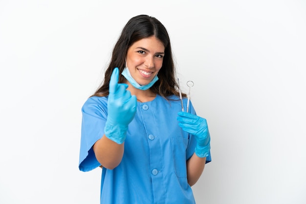 Mujer dentista sosteniendo herramientas sobre fondo blanco aislado haciendo gesto de venida