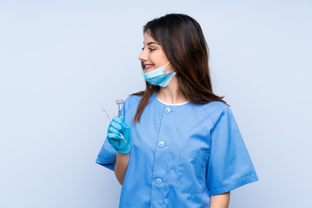 Mujer dentista sosteniendo herramientas sobre pared azul aislado mirando hacia el lado