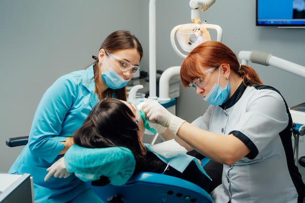 Mujer dentista y su asistente en ropa médica tratando los dientes del paciente en un centro estomatológico.