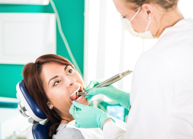 Mujer dentista con taladro dental reparando diente en el paciente femenino en la oficina.