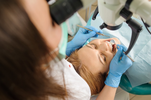 Mujer dentista tratando caries con microscopio en la oficina del dentista