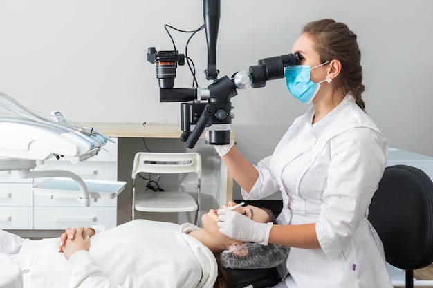 Foto mujer dentista usando microscopio dental tratando los dientes del paciente en la oficina de la clínica dental medicina odontología y concepto de atención médica equipo dental