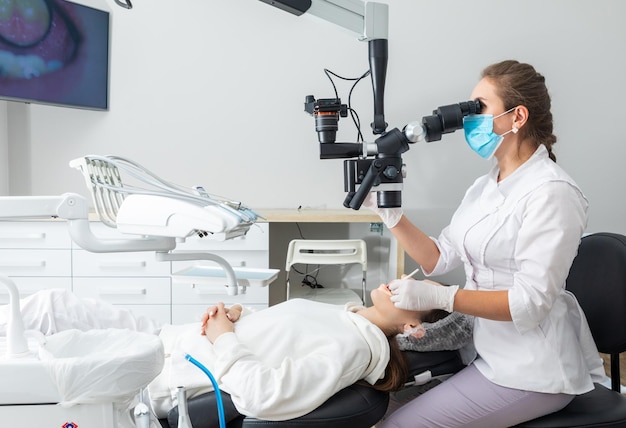 Mujer dentista usando microscopio dental tratando los dientes del paciente en la oficina de la clínica dental Medicina odontología y concepto de atención médica Equipo dental