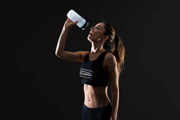 Mujer del deporte con una botella de agua en fondo oscuro