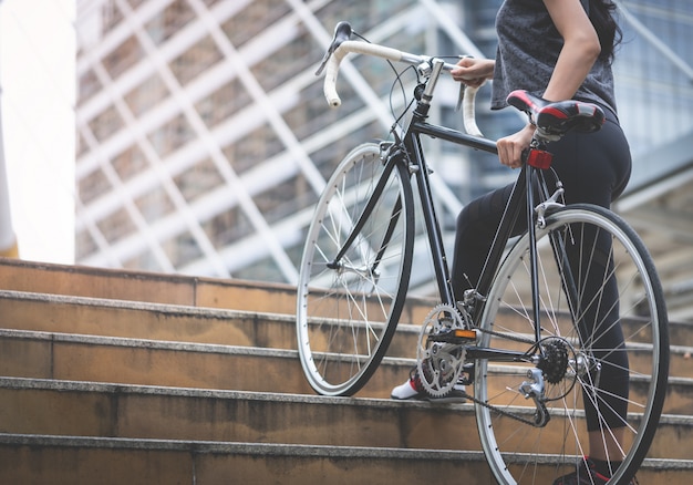 La mujer del deporte está llevando su bicicleta encima de la escalera