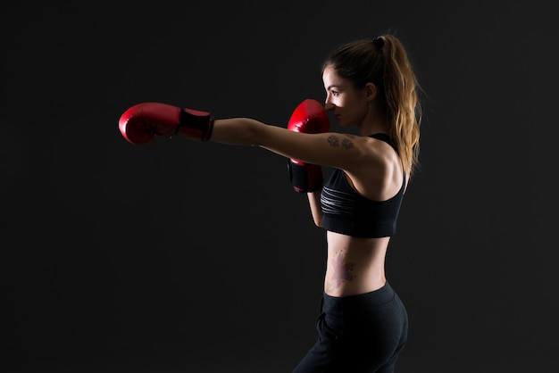 Mujer del deporte con los guantes de boxeo en fondo oscuro