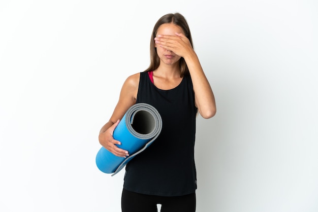 Mujer de deporte que va a clases de yoga mientras sostiene una estera sobre fondo blanco aislado cubriendo los ojos con las manos. No quiero ver algo