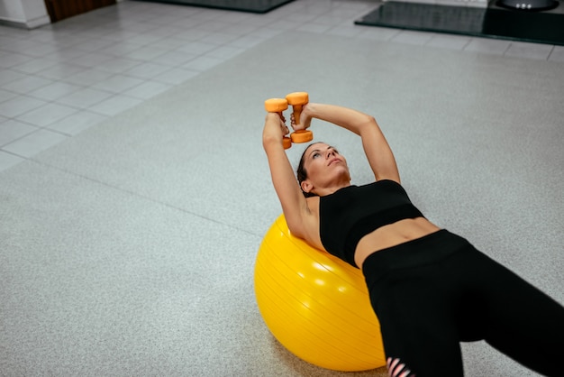 Mujer del deporte que ejercita con una bola y pesas de gimnasia de los pilates.