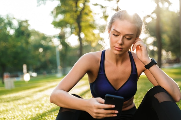 Foto mujer de deportes en el parque al aire libre escuchando música con auriculares mediante teléfono móvil.