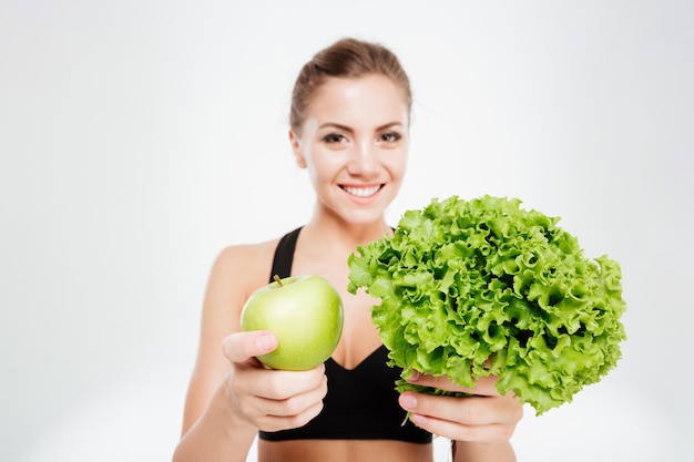 Mujer de deportes sonriente emocionada mostrando lechuga y manzana verde aislado