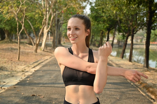 Mujer deportista saludable estirando los brazos para calentarse antes de hacer ejercicio en el parque Entrenamiento físico y concepto de estilo de vida saludable