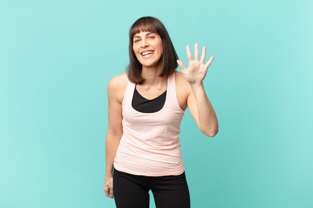 Mujer deportista sonriendo y mirando amistosamente, mostrando el número cinco o quinto con la mano hacia adelante, contando hacia atrás