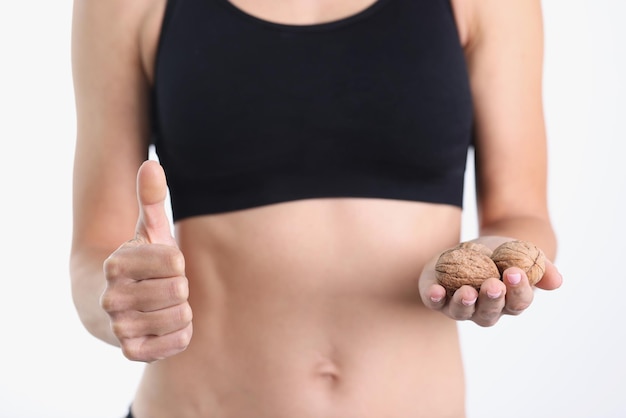 Mujer deportista sosteniendo nueces y pulgares arriba beneficios de las nueces para un concepto de figura delgada