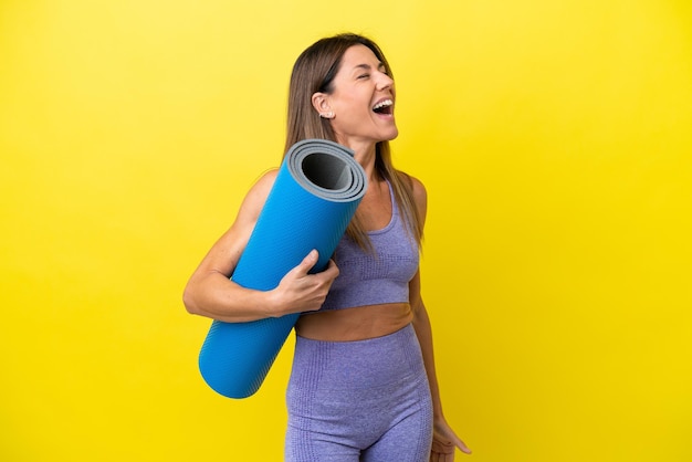Mujer deportista yendo a clases de yoga mientras sostiene una alfombra aislada de fondo no amarillo riéndose en posición lateral
