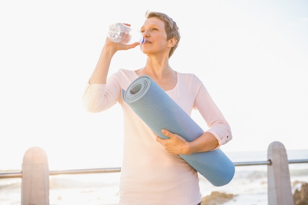 Mujer deportiva con agua potable estera de ejercicio