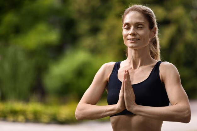 Mujer deportiva alegre que tiene meditación en el espacio de copia del parque