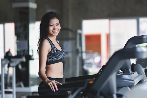 Mujer deportiva asiática corriendo en la cinta de correr en el gimnasio Entrenamiento cardiovascular Chico de estilo de vida saludable entrenando en el gimnasio Concepto de carrera deportiva