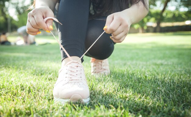 Mujer deportiva atar cordones de zapatillas antes de entrenar al aire libre. Preparándose para correr