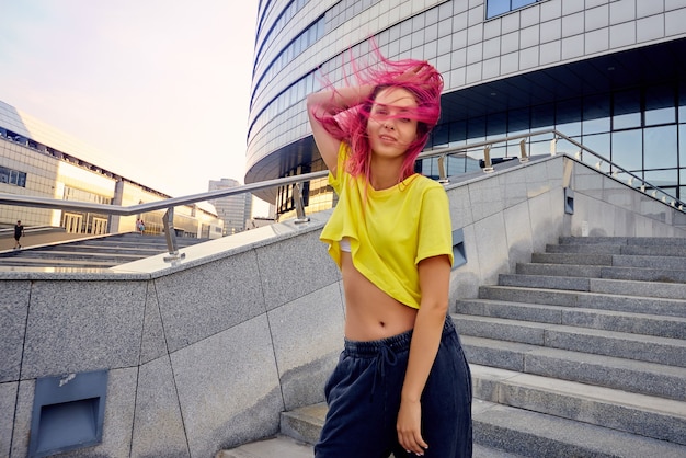 Mujer deportiva atlética con una camiseta amarilla y cabello teñido de rosa está bailando dinámicamente