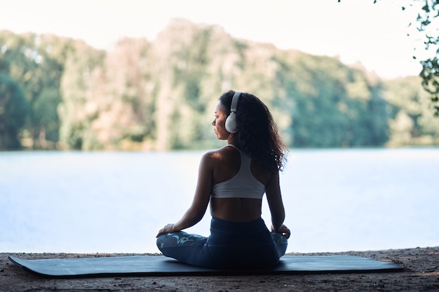 Mujer deportiva con auriculares meditando en posición de loto