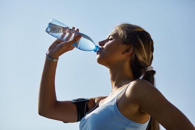 Mujer deportiva bebiendo agua contra el estadio.