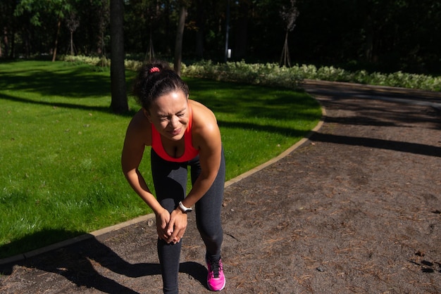 Mujer deportiva calambres en la pierna y siente dolor. Concepto de lesión de rodilla. Inflamación articular