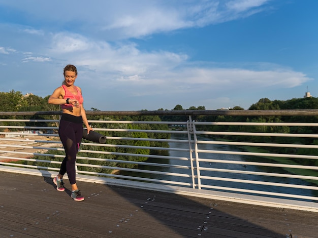 Mujer deportiva caminando mira su reloj inteligente en el centro de la ciudad