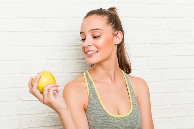 Mujer deportiva caucásica joven que sostiene una manzana