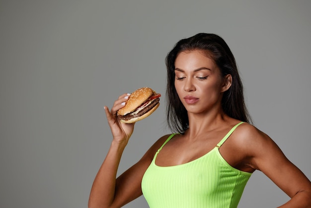 Mujer deportiva comiendo alimentos poco saludables sobre fondo claro Concepto de dieta