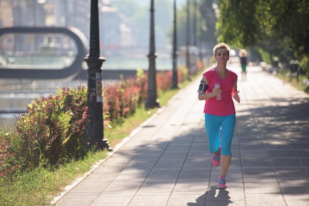 mujer deportiva corriendo en la acera temprano en la mañana con la escena del amanecer de la ciudad en segundo plano