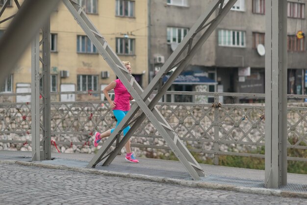 mujer deportiva corriendo en la acera temprano en la mañana con la escena del amanecer de la ciudad en segundo plano