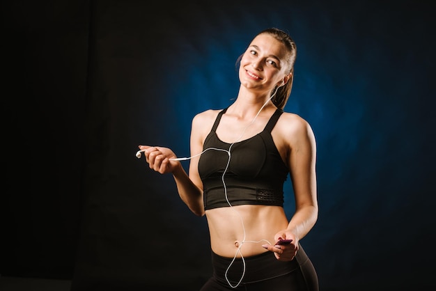 Mujer deportiva delgada con auriculares en el fondo negro del estudio