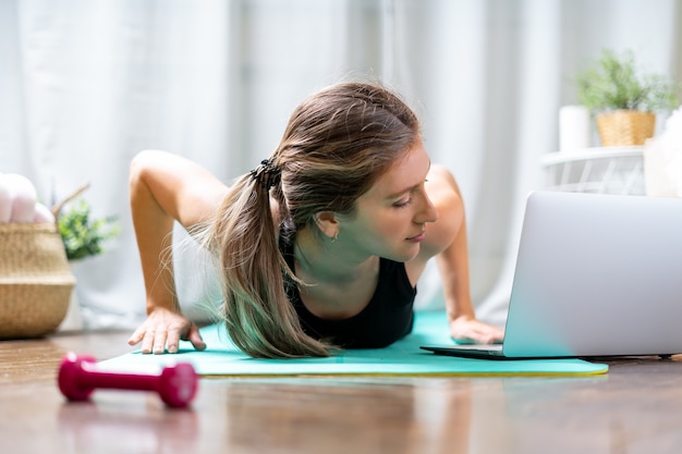 Una mujer deportiva con entrenamiento tutorial en línea portátil en casa