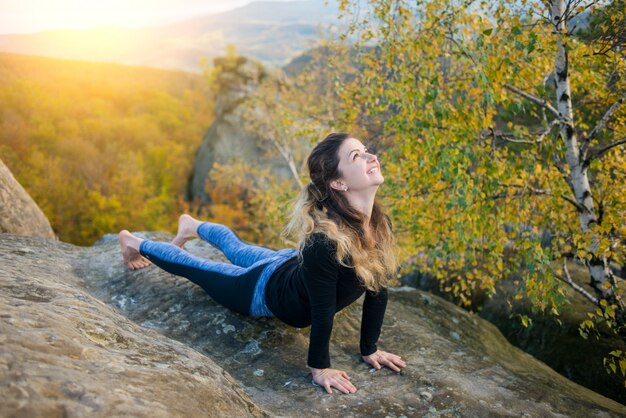 La mujer deportiva está practicando yoga en la cima de la montaña.