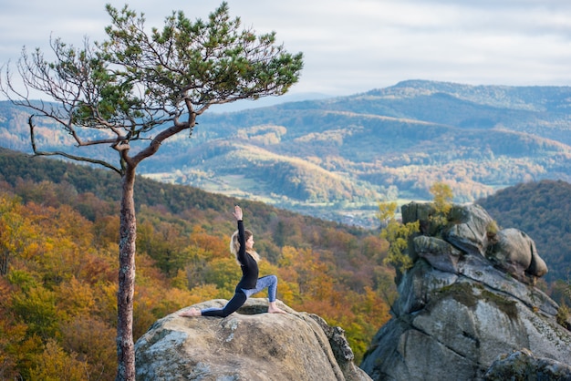 La mujer deportiva está practicando yoga en la cima de la montaña.